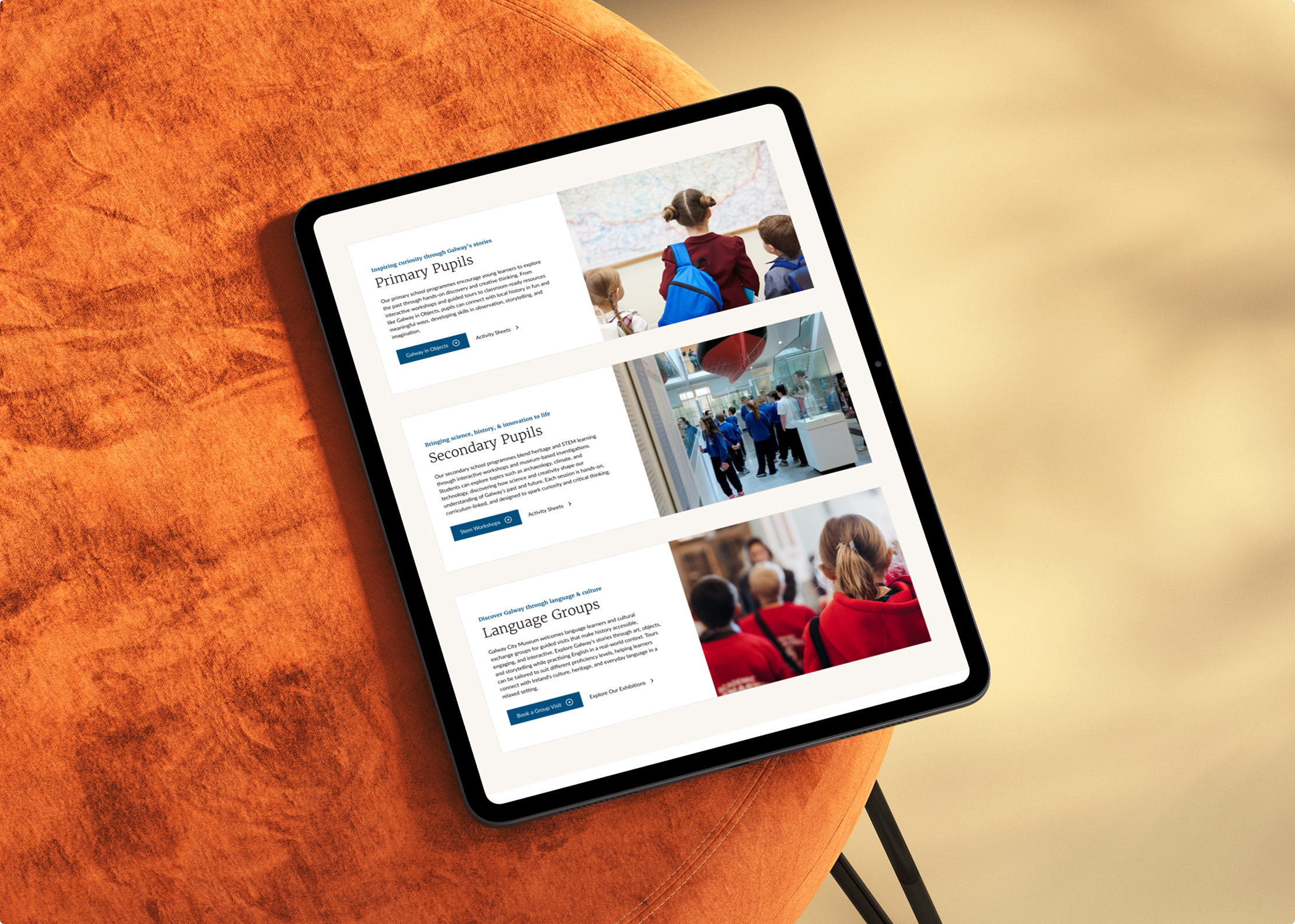 A tablet on an orange cushion displays a Simpl by Rob&Paul website with sections for Primary Pupils, Secondary Pupils, and Language Groups, each featuring a title, text, and photos of children in school settings.