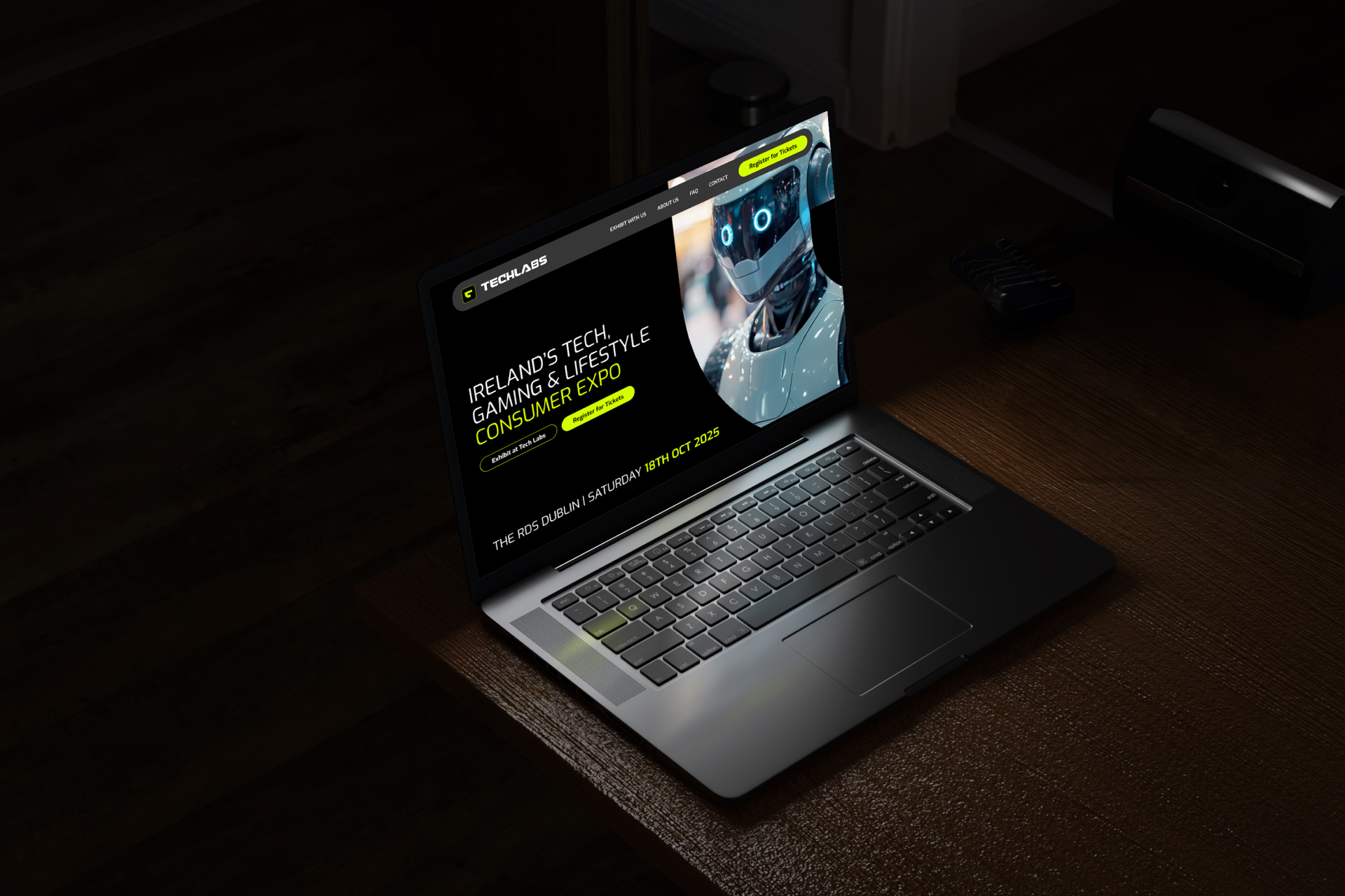 A laptop on a wooden desk displays a website for Irelands Tech, Gaming & Lifestyle Consumer Expo, with a futuristic robot image and event details highlighted on the screen.