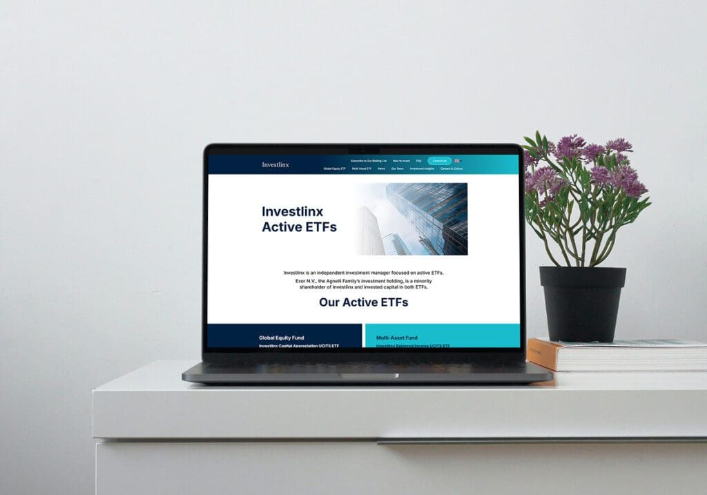 A laptop on a white desk displays the Investlinx Active ETFs webpage. Next to the laptop is a black potted plant with purple flowers and a stack of white books.