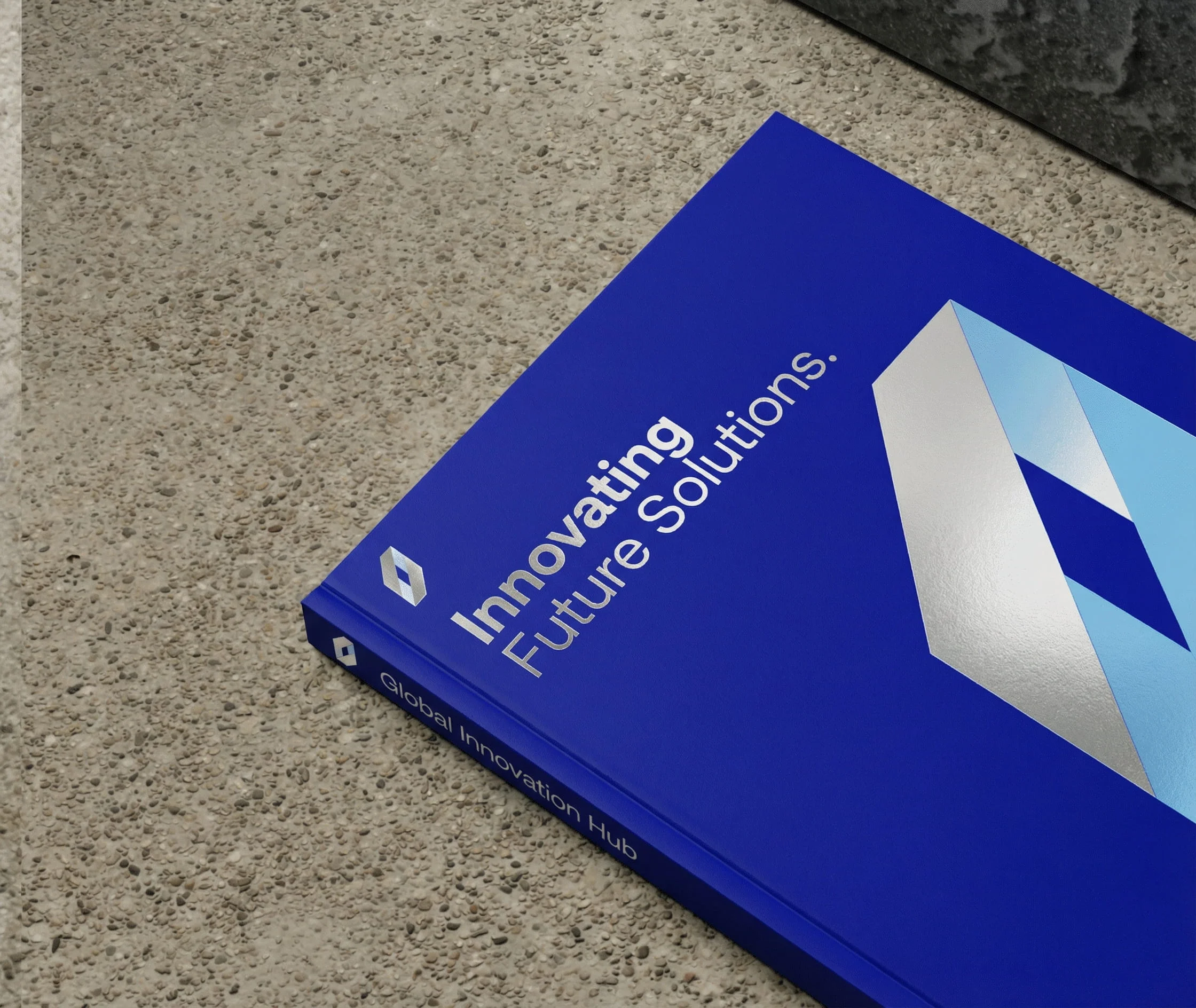 A blue hardcover book titled Innovating Future Solutions, featuring a geometric logo on the cover and Simpl by Rob&Paul branding, lies on a textured stone surface. The spine reads Global Innovation Hub.