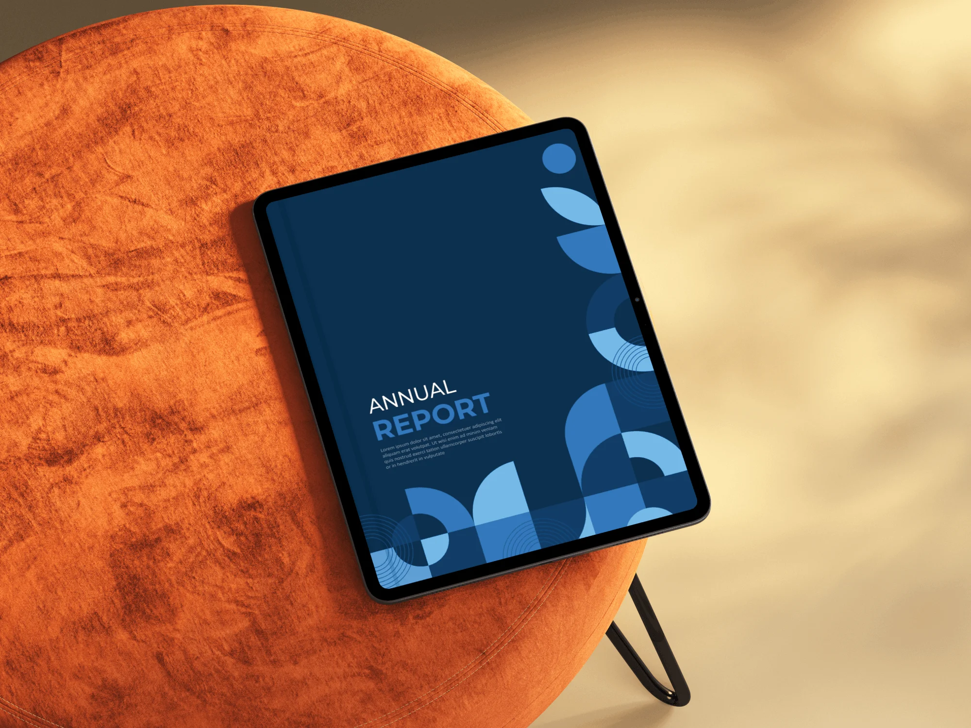 A tablet displaying a blue cover titled Annual Report with abstract blue patterns by Simpl by Rob&Paul rests on an orange, round, velvet chair against a softly blurred beige background.
