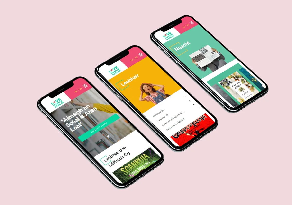 Three smartphones display colorful Simpl by Rob&Paul mobile app screens in Irish, featuring news articles, categories, and images, positioned on a light pink background.