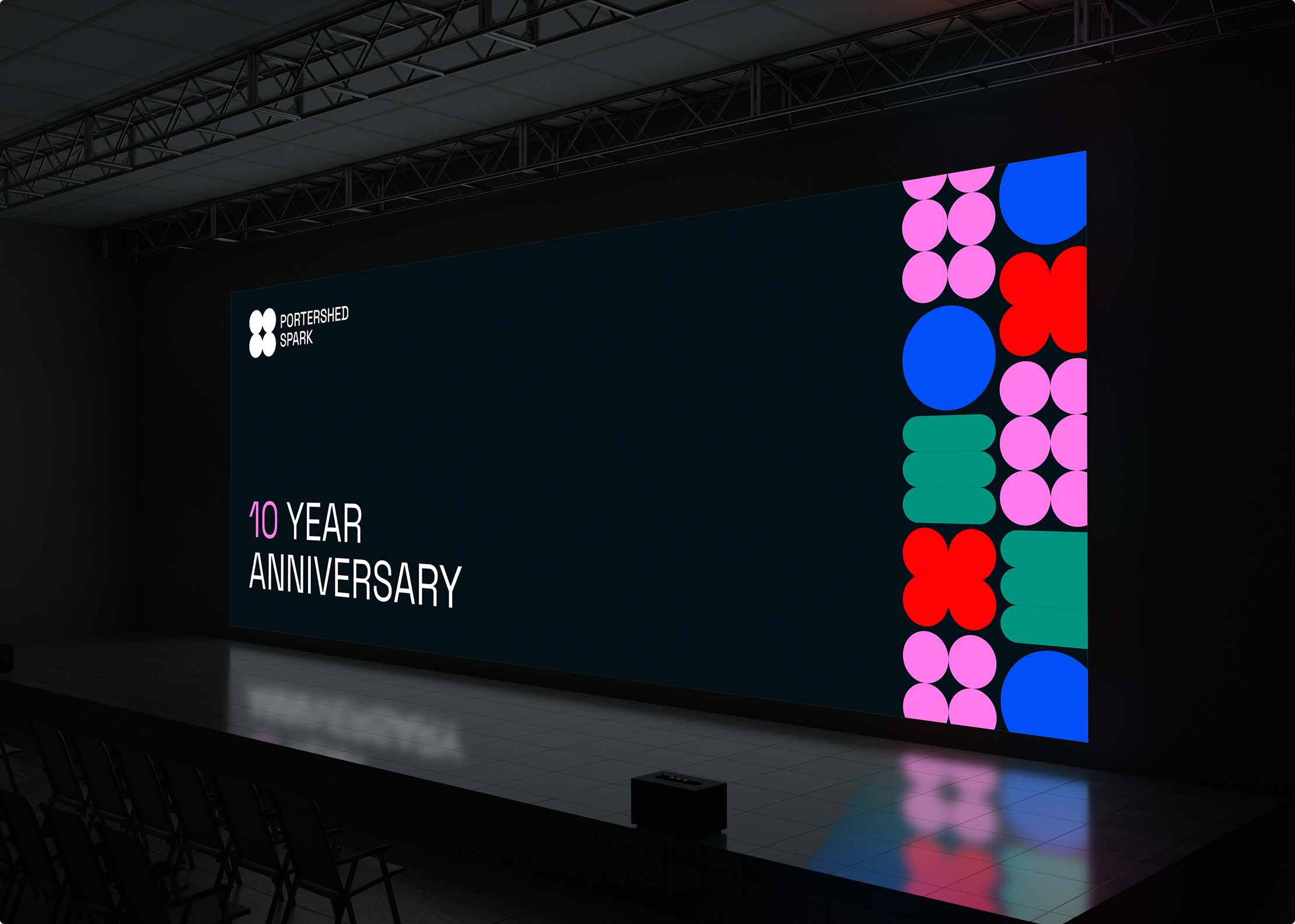 A dark stage with a large screen displaying 10 Year Anniversary and colorful geometric shapes on the right, featuring the PORTSHED SHARK logo and text in the top left, powered by Simpl by Rob&Paul.