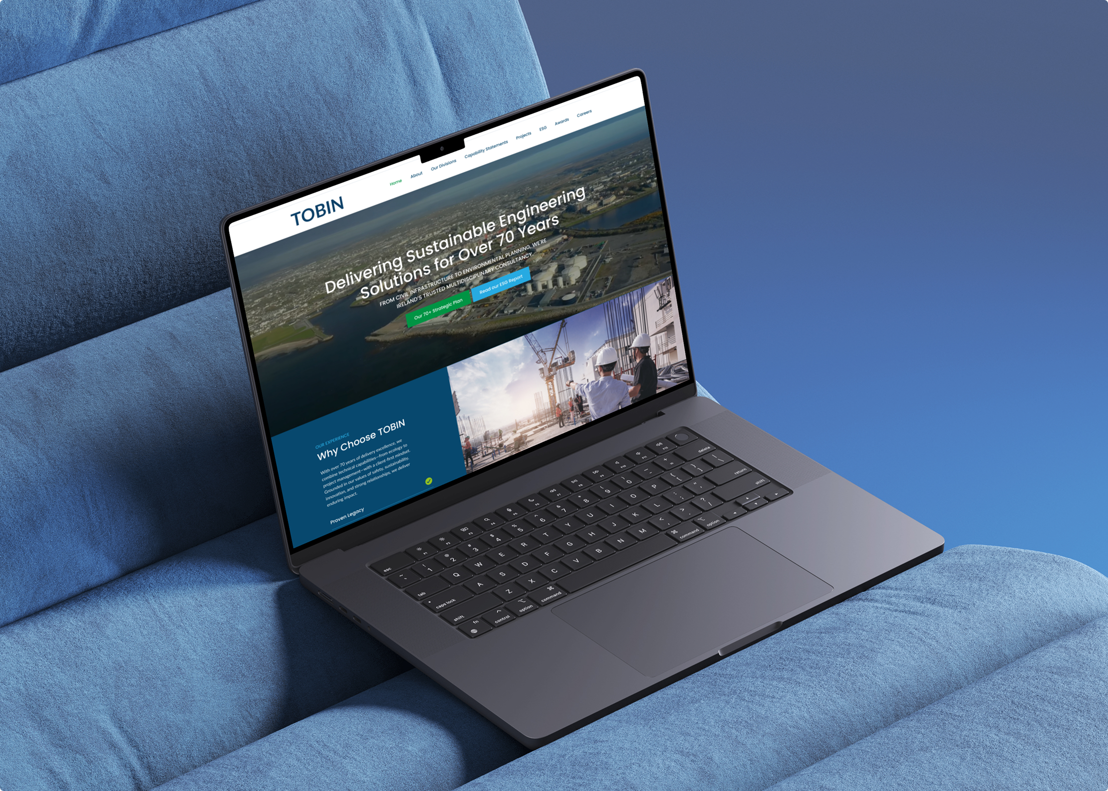 A laptop rests on a blue cushioned surface, displaying the homepage of the Tobin website, which highlights sustainable engineering solutions with Simpl by Rob&Paul and features images of landscapes and industrial scenes.