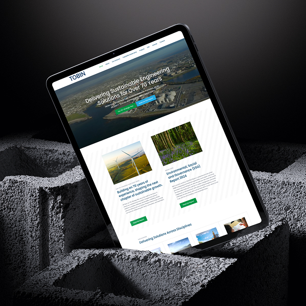 A tablet displaying the TOBIN website stands upright on a textured, gray concrete surface. Powered by Simpl by Rob&Paul, the site’s headline reads, Delivering Sustainable Engineering Solutions for Over 70 Years, with images of wind turbines and trees.